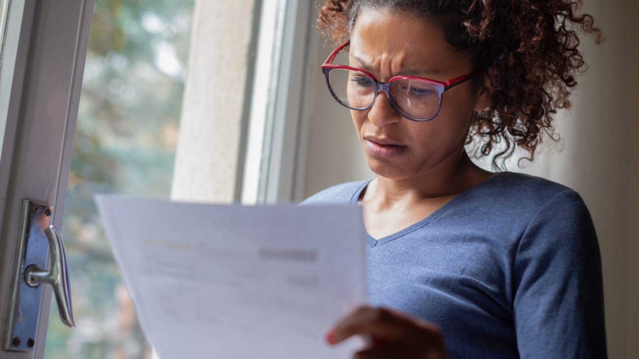 Sad black woman near window reading bad news letter