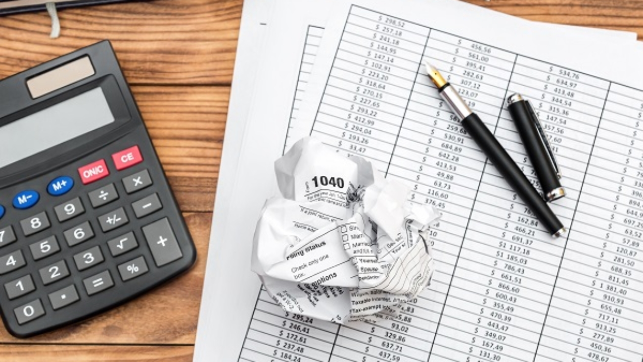 Crumpled tax form with financial documents, calculator and notepad on the table. Top view. Business concept.