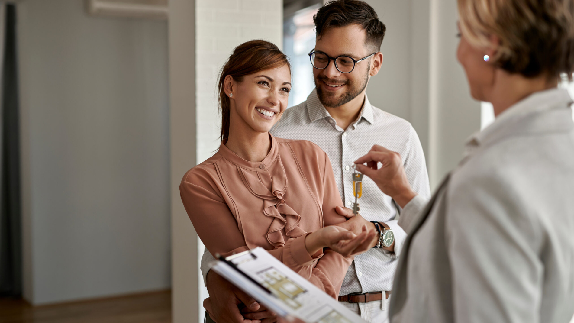 Happy couple buying new home and receiving house keys form real estate agent.