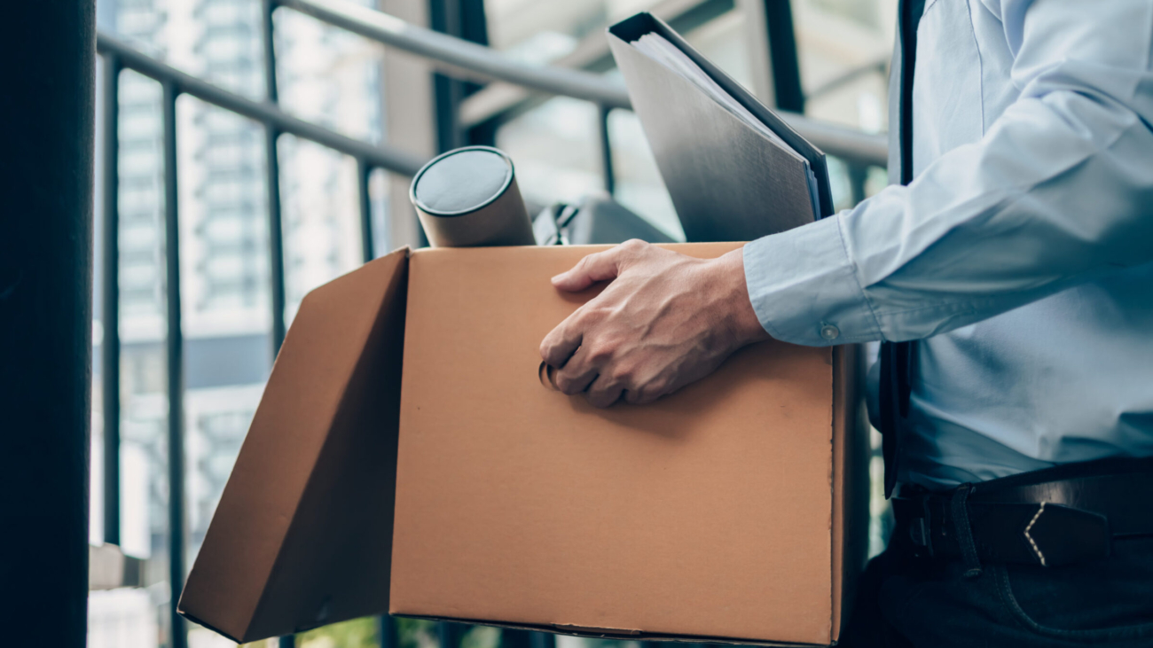 Unemployed hold cardboard box and laptop bag, dossier and drawing tube in box. Quitting a job, businessman fired or leave a job concept.